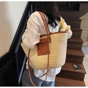 Detail of a large woven straw tote bag featuring brown leather trim and metal accents
