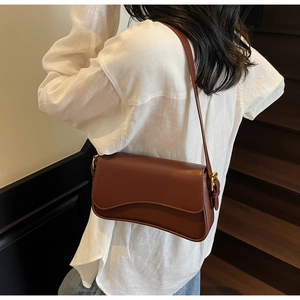 Sac sous le bras en cuir caramel avec rabat ondulé et boucles dorées porté par un mannequin