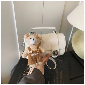 Detail of white box handbag with metal twist lock and cute teddy bear charm on books
