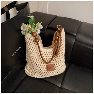 Detail of woven tote bag with brown leather strap and wooden bead accents on black sofa