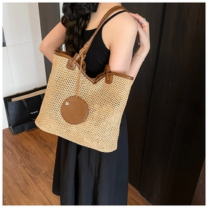 Detail of woven straw tote bag with brown leather trim and circular pendant accessory