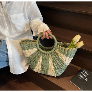 Detail of green and cream woven straw handbag with gold metallic trim and round handles