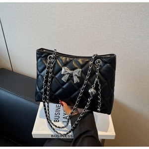 Detail of black quilted chain bag featuring a silver bow metal charm and chain strap