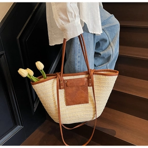 Detail of hand-woven straw tote bag with brown leather trim and pocket on city stairs