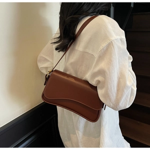 Gros plan d'un sac porté épaule en cuir marron avec boucle dorée sur une chemise