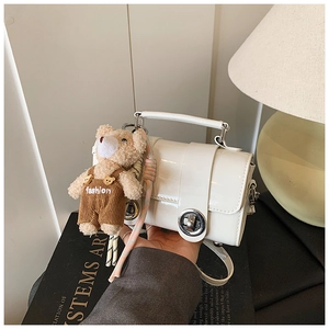 Close-up of white patent leather mini pillow bag with cute teddy bear charm and silver clasp