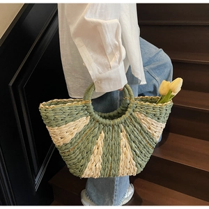 Detail of handwoven straw tote featuring green and white color-block patterns with gold accents