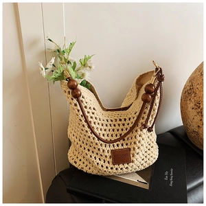 Detail of beige crochet tote bag with wooden bead straps and brown leather brand logo
