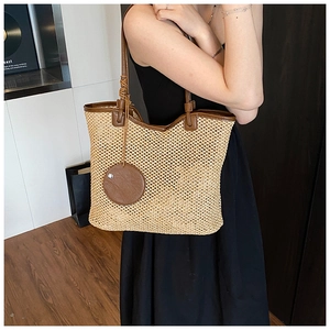 Detail of woven straw tote bag with brown leather trim and circular tag on shoulder