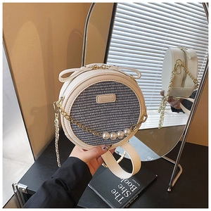 Detailed shot of woven round crossbody bag with pearl strap and golden chain accents