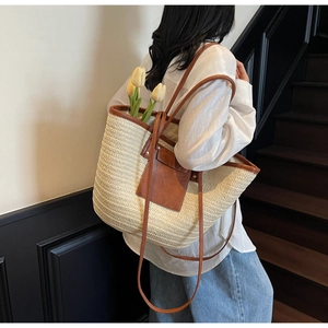 Detail of large woven straw tote bag with brown leather trim and slim shoulder strap