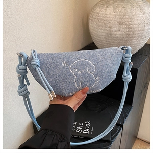 Détail du sac croissant en denim bleu avec broderie chiot et fermeture éclair argentée