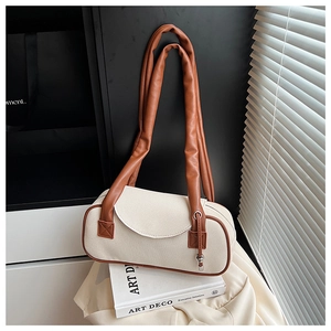 Dettaglio della borsa in tela con finiture in pelle marrone e ciondolo in metallo sulla tracolla