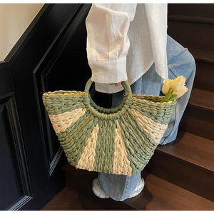 Detail view of woven straw tote bag with green contrast stripes and gold thread accents
