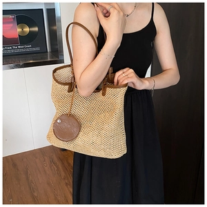 Detail of hand-woven straw tote with brown leather trim and slim shoulder straps