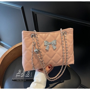 Detail of pink quilted shoulder bag featuring silver bow hardware and metal chain strap