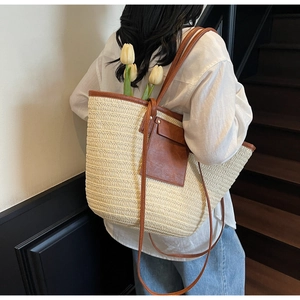 Detail of a large woven straw tote bag featuring brown leather trim and a front pocket