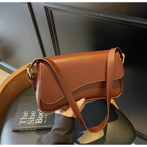 Détail du sac sous l'aisselle en cuir marron foncé avec rabat ondulé et boucles dorées chic
