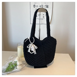 Detail of black hand-knitted tote bag featuring a pearl doll charm and thick crochet texture