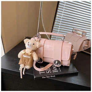 Detailed close-up of a pink glossy bag with a metal twist lock and cute plush bear charm