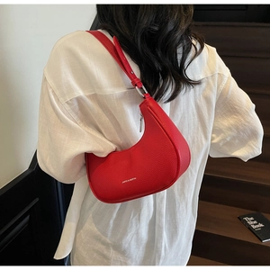 Close-up of red lychee grain leather crescent bag worn over a white linen shirt