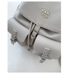 Close-up of light grey lychee pattern leather backpack with PAN 'TOR metal logo and buckle