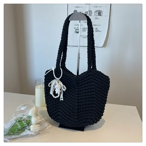 Detail of black hand-woven tote bag featuring a pearl charm and lace bow accessory