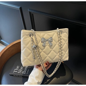 Close-up of white quilted crossbody bag with silver bow accent and metal ball charm