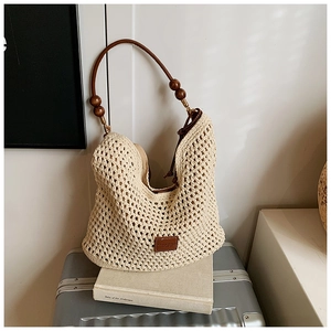 Detail view of cream woven tote bag with dark brown leather straps and wooden bead accents