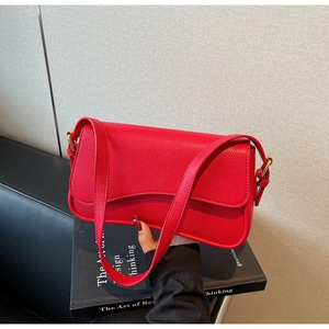 Detail shot of a bright red lychee texture leather shoulder bag with gold metal buckle