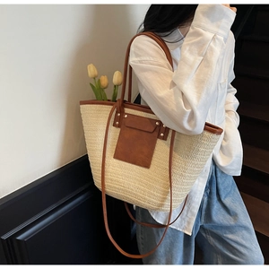 Detail of a large woven straw tote bag with brown leather straps worn by a model