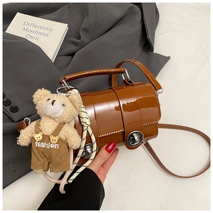 Detail of a brown patent leather mini barrel bag with a plush bear charm and metal clasp