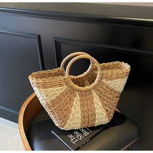 Detail of hand-woven straw tote with golden thread accents on textured brown and beige stripes