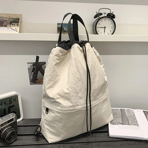 Detail der cremeweißen Kordelzug-Tasche mit Nylon-Textur und Reißverschlussfach vorne