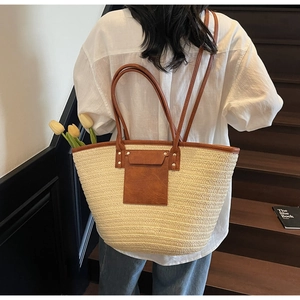 Close-up of a large straw tote bag with brown leather accents on a wooden staircase