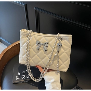 Macro shot of white quilted leather bag with silver metal bow and chain strap details