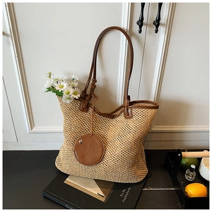 Detail of woven straw tote bag with brown leather handles and a round hanging coin purse