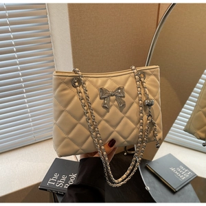 Detail of cream quilted tote bag with silver bow accent and metal chain strap