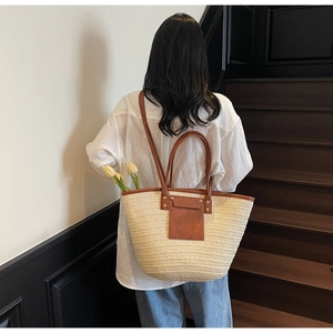 Detail of large straw tote bag with brown leather handles worn by model on white background