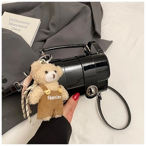 Detail of black patent leather bag with silver rotary buckle and cute bear charm