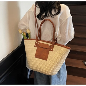 Close-up of large woven straw tote bag with brown leather trim and metal rivet details