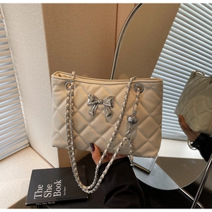 Close-up of a white quilted crossbody bag featuring a silver metal bow and chain strap