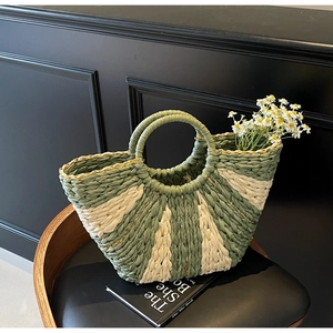 Detail of green and beige woven straw bag with dual handles on a wooden chair