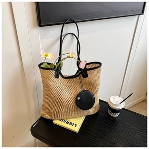 Close-up of woven straw tote bag with black leather trim and round zipper pouch charm
