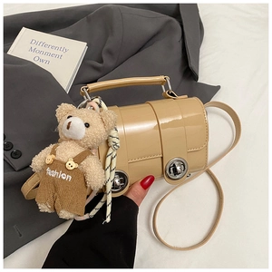 Detail of light khaki glossy crossbody bag with bear charm and silver twist lock
