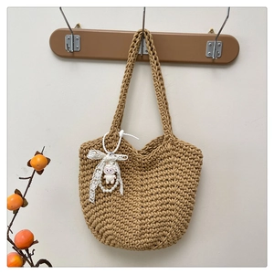 Detail of hand-woven bucket bag featuring a white plush charm with lace bow and pearl accent