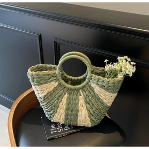 Detail of handwoven fan-shaped straw tote with green contrast stripes and round handle
