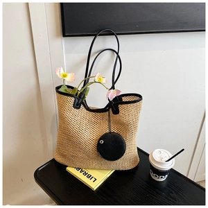 Close-up of woven straw tote bag featuring black leather trim and mini round pouch