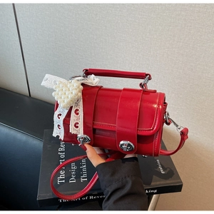 Dettaglio borsa a cilindro rossa lucida con perle a cuore e ciondolo fiocco in pizzo