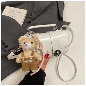 Detail of white glossy patent leather bag with silver buckle and cute bear pendant